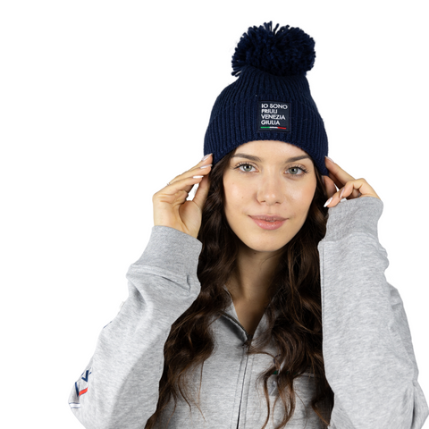 Berretto blu con pon pon blu e logo Io Sono Friuli Venezia Giulia indossato su sfondo bianco