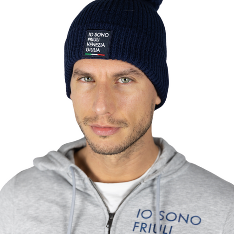 Berretto blu indossato da un uomo con logo Io Sono Friuli Venezia Giulia e felpa grigia coordinata su sfondo bianco